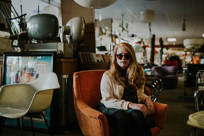 a portrait of a girl sitting in an armchair in a thrift shop