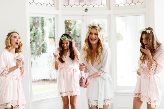 bride and bridesmaids in pink robes opening champagne