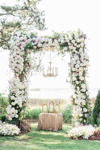 wedding altar decoration arch of white flowers with an altar and a golden chandelier with candles aj dunlap via instagram