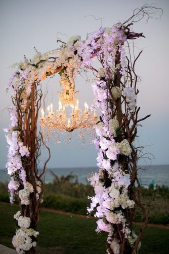 wedding altar decoration arch with wooden branches orchid flowers with elegant chandelier sara kauss photography via instagram